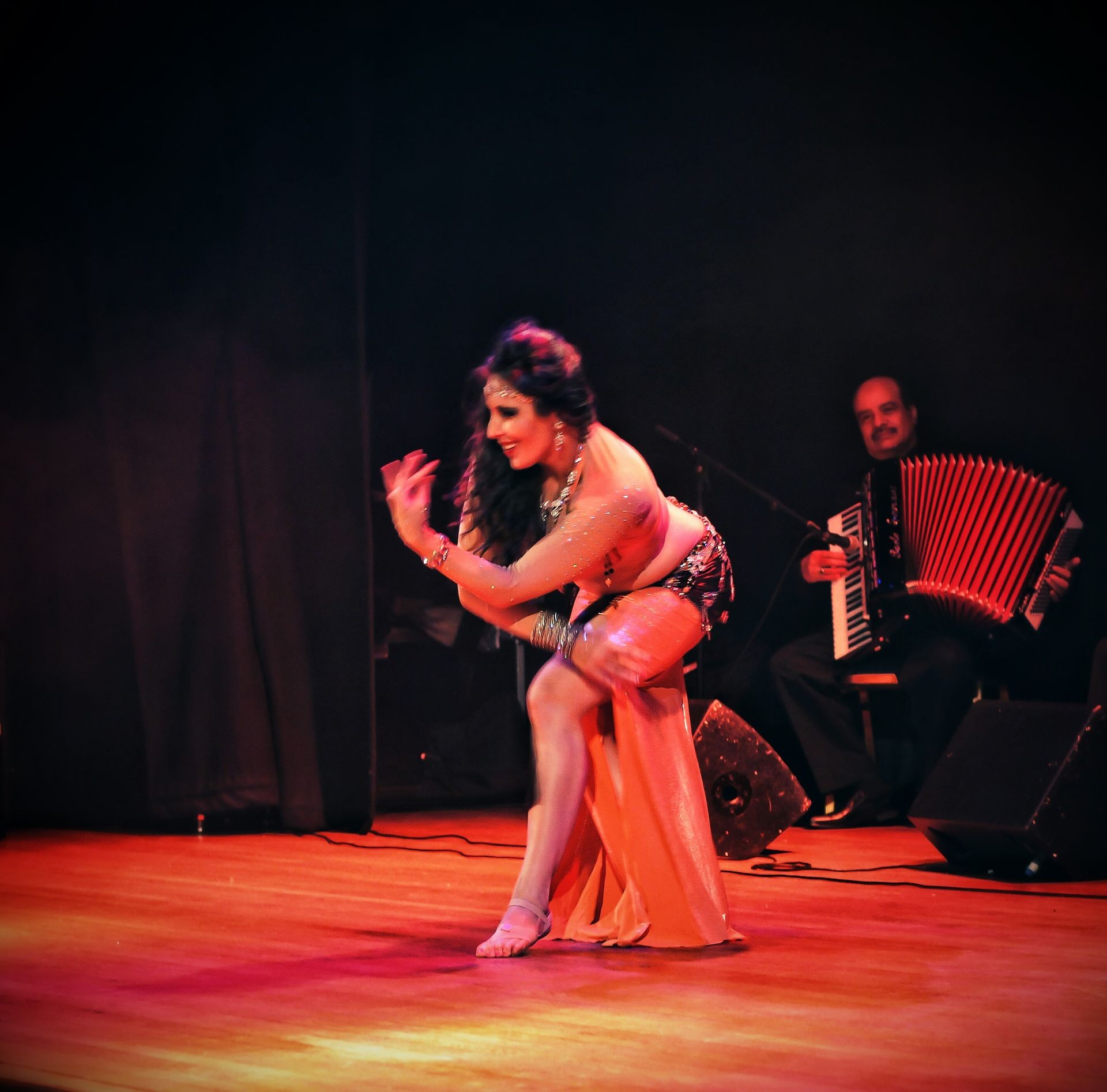 Dancer performing on stage with accordion musician in the background, under colorful stage lights.