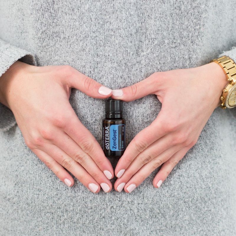 Hands making a heart shape around a bottle of doTERRA essential oil against a gray sweater.